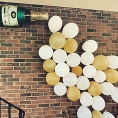 white and gold balloons are hanging on the brick wall next to a bottle of champagne