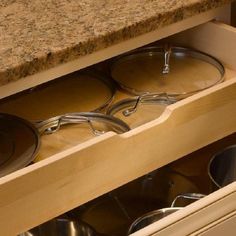 pots and pans are stored in the drawers of a kitchen cabinet with granite counter tops