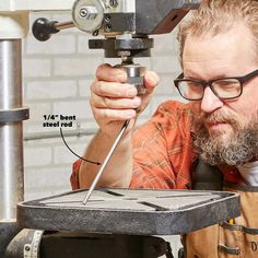 a man in glasses is working on an object with a drill and some metal tools