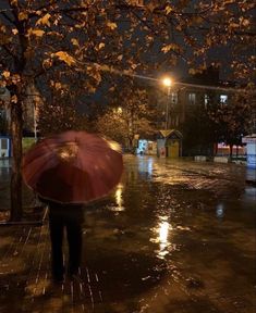 a person with an umbrella walking in the rain on a city street at night time