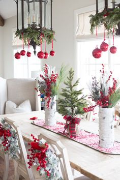 a dining room table decorated for christmas with red ornaments and greenery in vases