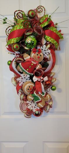 a christmas wreath on the front door with ornaments hanging from it's sides and ribbons