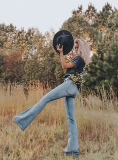 a woman with blonde hair wearing jeans and a cowboy hat is posing in a field