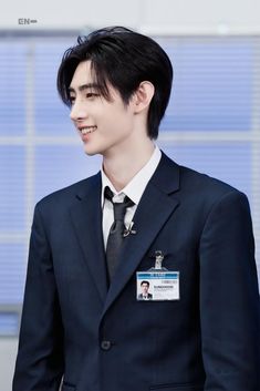 a young man in a suit and tie smiles at someone else's name tag on his lapel