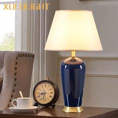 a blue lamp sitting on top of a wooden table next to a cup and clock