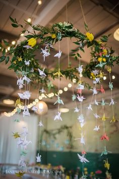 some paper birds hanging from the ceiling in a room with flowers and greenery on it