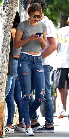 a woman in ripped jeans looking at her cell phone while standing next to other people