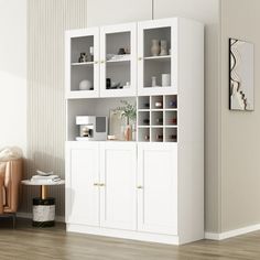 a white bookcase with glass doors and shelves in the corner next to a chair