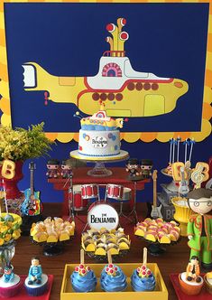 a birthday party with cupcakes, cakes and decorations on a table in front of a yellow submarine