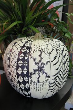 a black and white pumpkin sitting on top of a table next to a potted plant