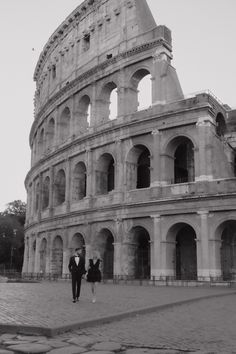 a man and woman standing in front of an old roman colossion, black and white