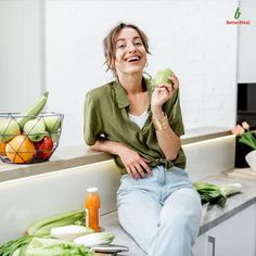 a woman sitting on a counter with vegetables and fruit in front of her smiling at the camera