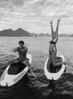 two women on surfboards in the water with their arms up and one holding her head