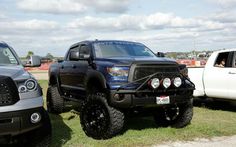 two pickup trucks parked next to each other in a grassy area with people looking at them