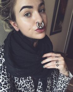 a woman with piercings on her nose wearing a leopard print shirt and black scarf