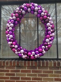 a wreath made out of purple and silver ornaments hanging on a brick wall in front of a window