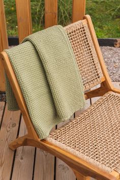 a wooden chair with a green towel on it's back and two other chairs in the background