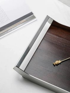 a metal and wood tray with a key on it next to an open book that is sitting on a table