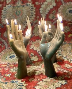 three ceramic hands holding lit candles on a rug