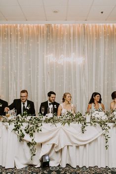 a group of people sitting at a table with flowers and greenery in front of them