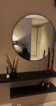 there is a mirror on the wall above a shelf with candles and vases in front of it