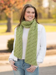 a woman wearing a green knitted scarf standing in front of a tree with her hands on her hips