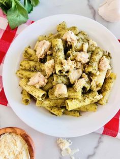 a white bowl filled with pasta and chicken on top of a red and white checkered table cloth