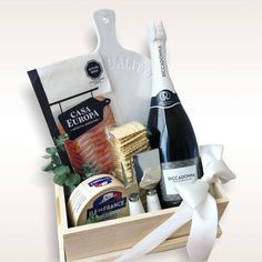 a wooden box filled with cheese, wine and other items next to a white ribbon