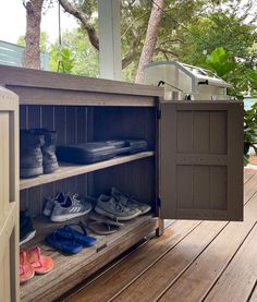 an outdoor shoe rack with several pairs of shoes in it on a wooden deck next to trees