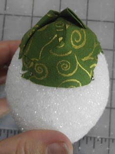 a hand is holding a green and white snowball with gold designs on it's side