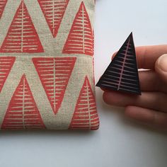 a hand holding a small black triangle on top of a red and white pillow next to a piece of fabric