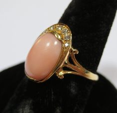 This lovely coral ring is finely crafted in 18K yellow gold. In bands interior is hallmarked 750 and has been tested to ensure the golds purity. Outer side of band is also hallmarked. Could be a makers mark or country. I believe it may be Swiss or Austrian? Not quite sure but closest I can find to it. Setting is adorn with a sweet angel skin coral cabochon. It measures 1/2 an inch by 3/8 of an inch. Surrounding the coral are brilliant eye clean diamonds. Almost in a crescent moon design. Overall Elegant Oval Coral Rings, Elegant Coral Oval Rings, Coral Elegant Wedding Rings, Elegant Coral Wedding Rings, Elegant Coral Ring Jewelry, Elegant Coral Rings For Anniversary, Formal Coral Ring, Crescent Moon Design, Diamond Angel