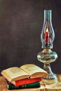 an open book sitting on top of a table next to a glass vase filled with a candle