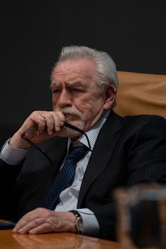 an older man sitting at a table with his hand on his chin and looking off to the side