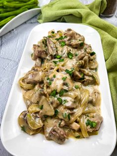 a white plate topped with pasta covered in mushroom sauce and green onions next to asparagus