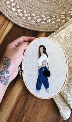 a woman's hand is holding a cross - stitch embroidery project with a girl in white shirt and blue pants