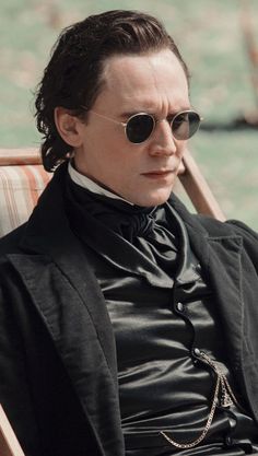 a man in a black suit and sunglasses sitting on a chair with his eyes closed