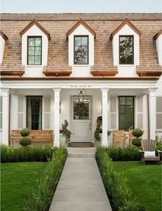 a white house with brown shingles and two benches in the front yard, along with green grass