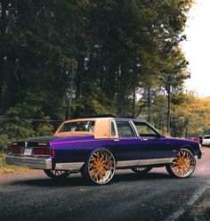 a purple car with gold rims parked on the side of the road in front of some trees