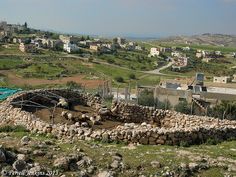 an old stone wall in the middle of a field with buildings and hills in the background