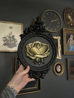 a person holding up a clock with a rose on it in front of several framed pictures