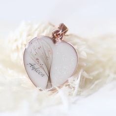 a white heart shaped pendant sitting on top of a pile of feathers with writing on it