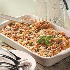 a casserole dish with pasta and vegetables in it on a table next to silverware