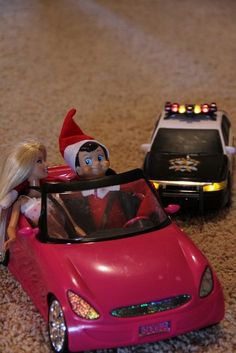 two toy cars are on the floor with an elf and a police car behind them