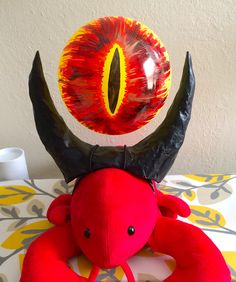 a red stuffed animal with horns and an eyeball on it's head sitting on a table