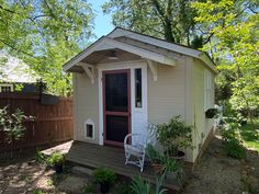 a small shed with a red door and white chair on the porch next to it