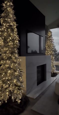 a white christmas tree sitting in front of a window next to a fireplace with lights on it