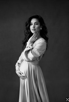 a woman in a long dress poses for a black and white photo with her hand on her chin