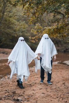 two people in white cloths walking down a dirt road with trees in the background