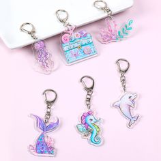 four keychains with different designs on them sitting next to a white box and pink background